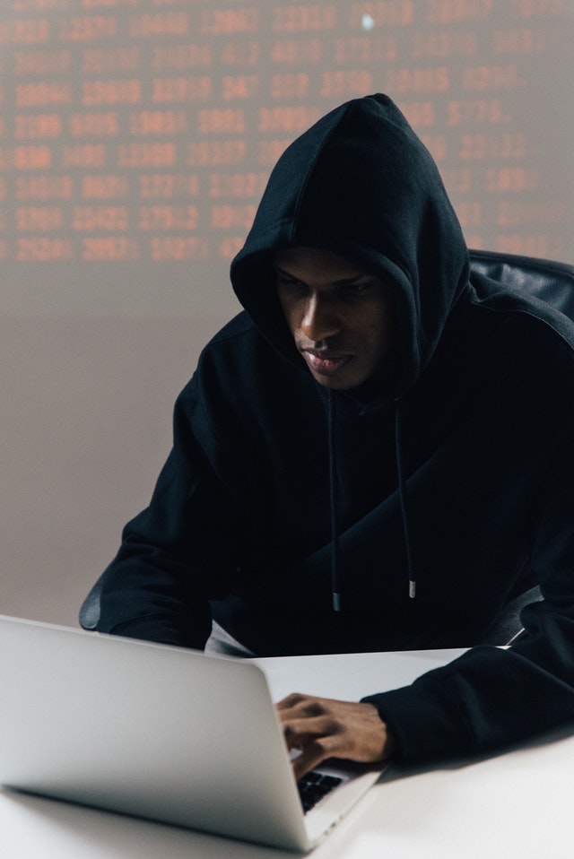 A man in a hood typing on a computer