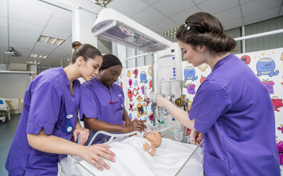 Midwifery students tending to a patient. They are wearing purple scrubs.