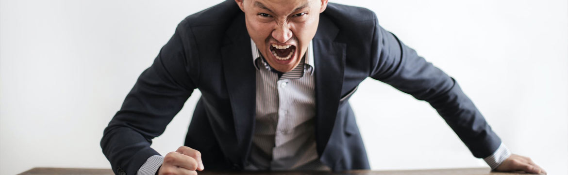 A man yelling and hammering his fist on a desk