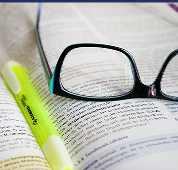A picture of some glasses and a highlighter resting on a book.