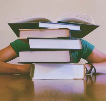 A student with their head on a desk behind a pile of books