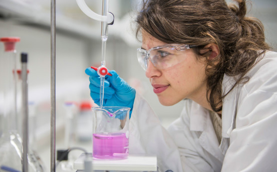 A female student with lab coat on and wearing goggles in lab
