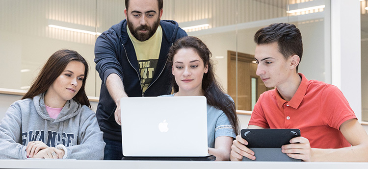 Two male and one female student gathered around a laptop