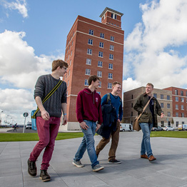 Group of male students walking in front of the Tower Information Centre on Swansea University's Bay Campus