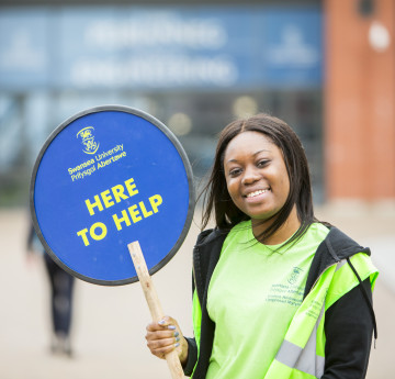 Student ambassador smiling with a 'Here to help' sign 