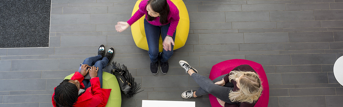 Aerial photo of three women sitting and chatting on colourful beanbags on a grey floor 