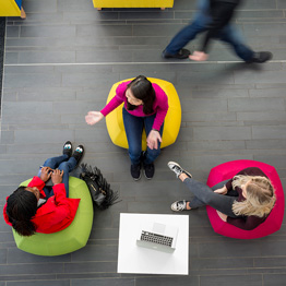 Aerial photo of three students sitting on colourful beanbags chatting