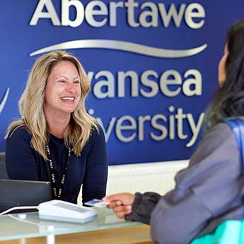 A female customer service staff member talking to a student at the reception desk on Singleton Campus