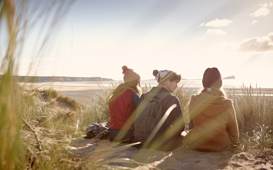 Three people sitting on beach wearing bobble hats