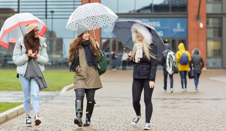 Students walking with umbrellas outside Engineering Central building on Bay Campus