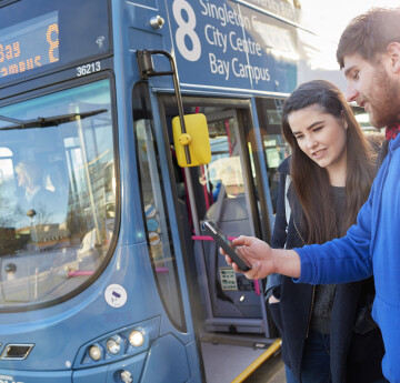 Male and female student looking at a mobile phone, about to get on a waiting bus