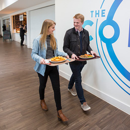 Two people walking through The Core restaurant carrying food on trays
