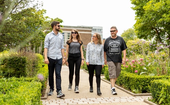 a group of four people walking side by side on a path surrounded by bushes 