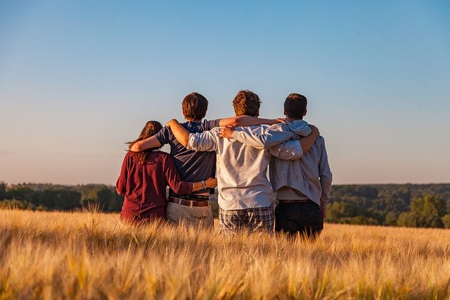 Four friends standing in a field facing away from the camera with arms around each other’s shoulders