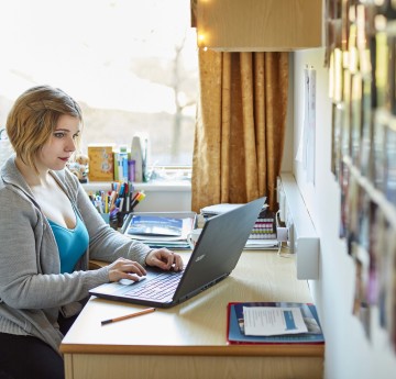 Student sitting at her desk in her student accommodation. She is working at her laptop.